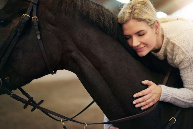 Close up of caring woman hugging her dark horse