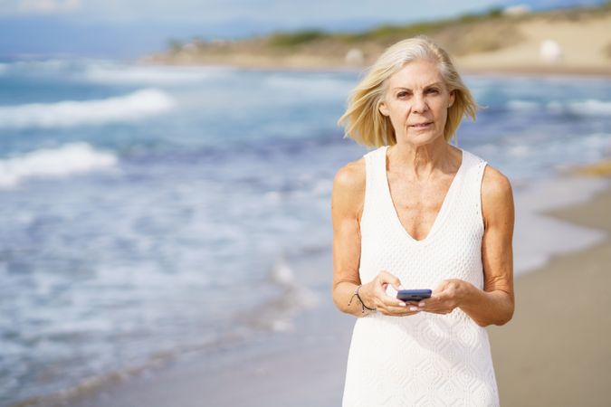 Serious older woman using her phone on a rocky beach