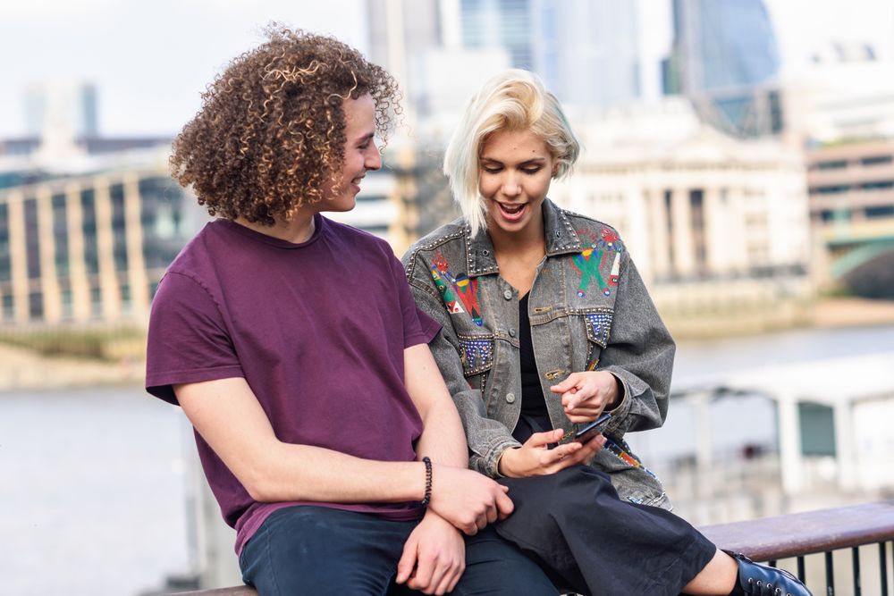 Happy couple sitting and talking with each other while on fence over river