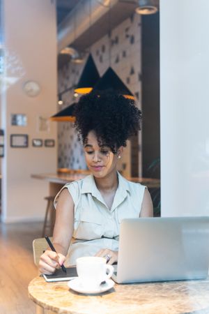 Smiling Black woman working on graphic tablet in cafe