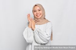 Muslim woman in headscarf and light blouse clapping and smiling 41L885