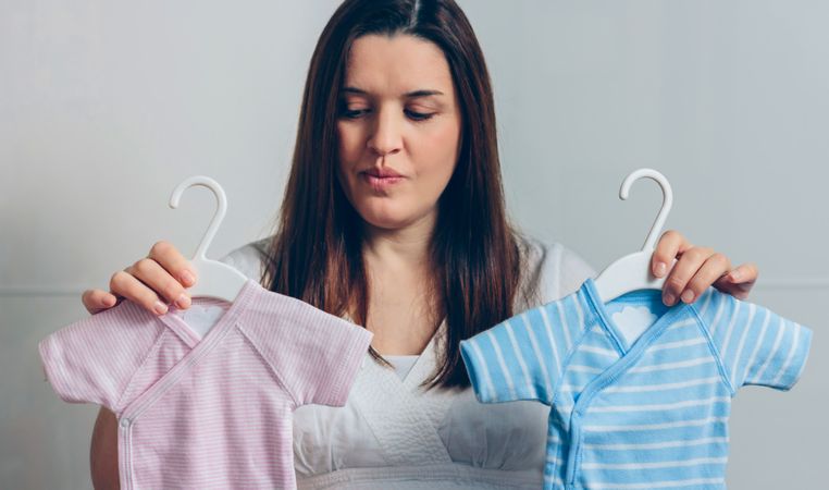 Pregnant woman choosing baby bodysuits