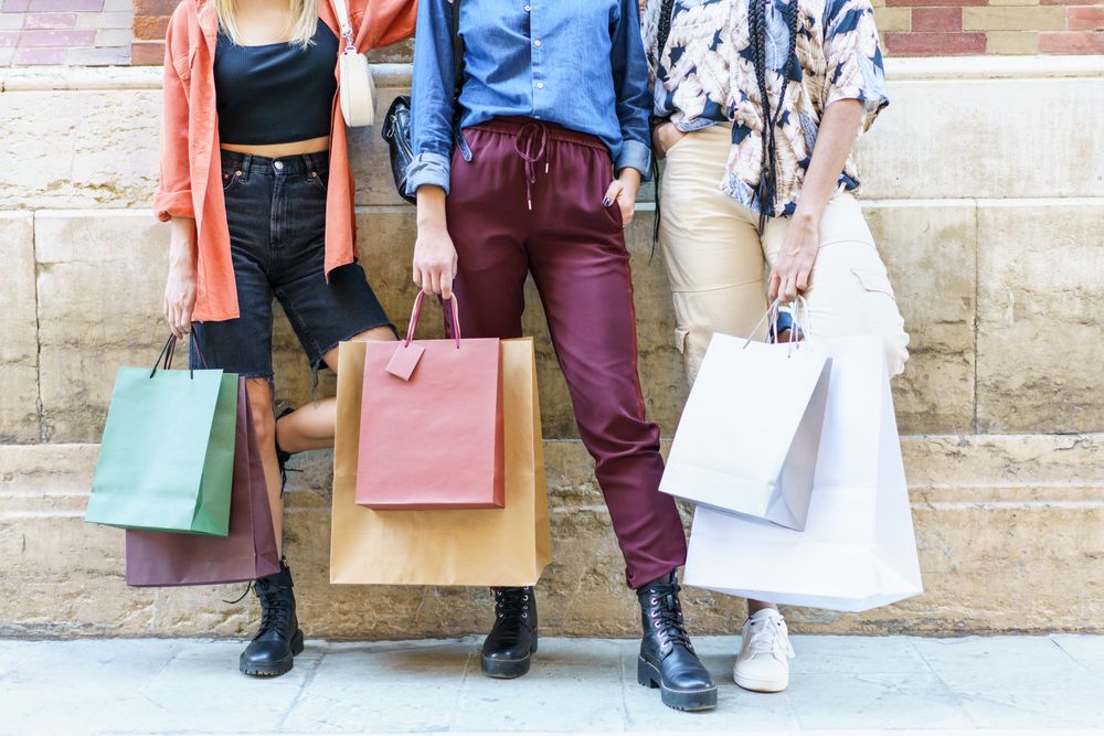 Cropped shot of three women with shopping bags against brick wall