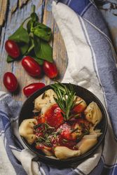 Bowl of delicious ravioli with tomato sauce and rosemary on shabby table
