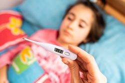Girl in bed with adult taking her temperature