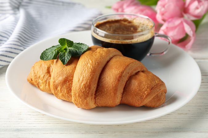 Plate with croissant on wooden table with tulips, close up