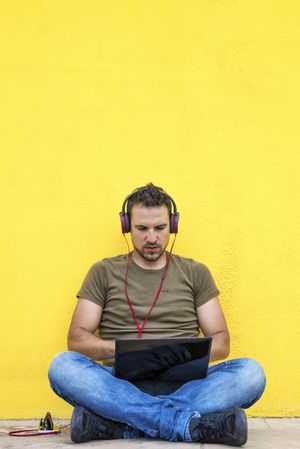 Male with red headphones sitting outside looking at laptop