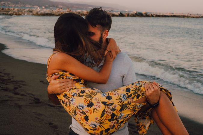 Amorous man carrying woman on arms along sandy beach