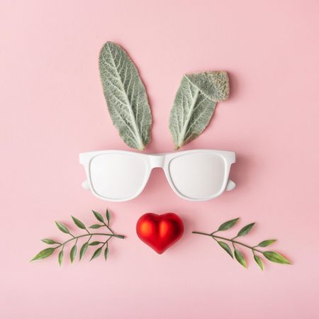 Bunny rabbit face made of natural green leaves with sunglasses and heart nose on pink background