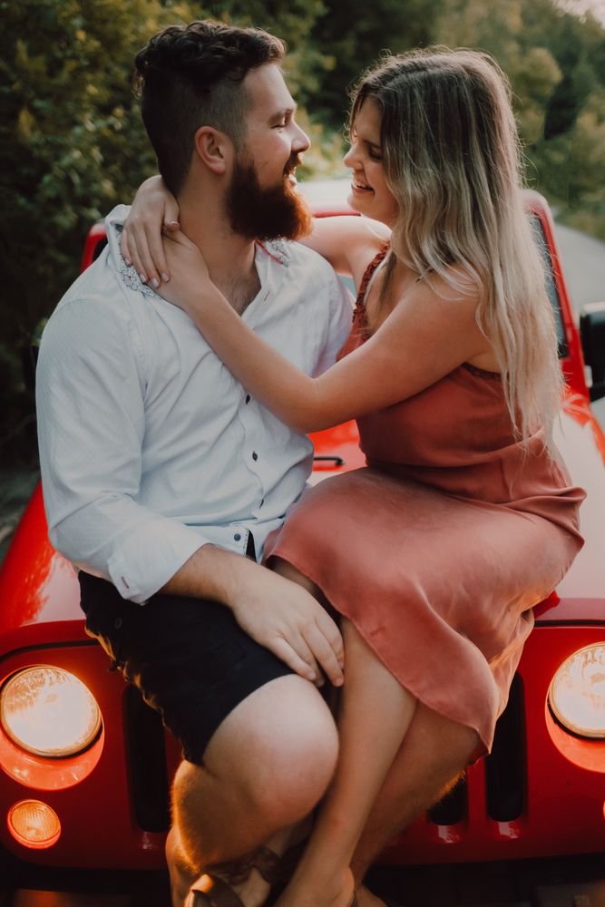 Loving couple sitting on car on road near forest