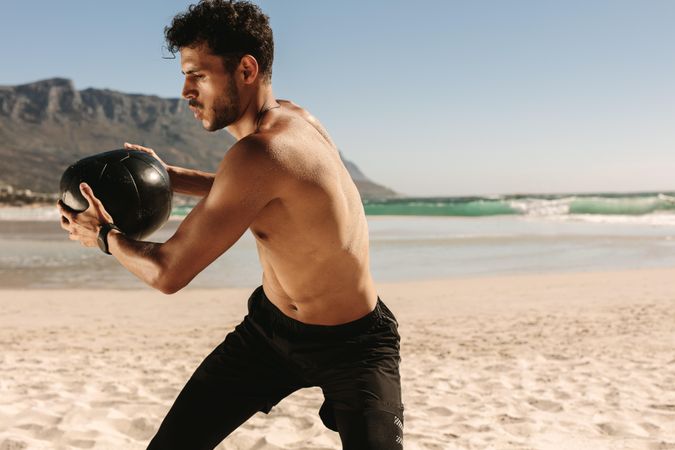 Fit male holding medicine ball and lunging to the side outdoors