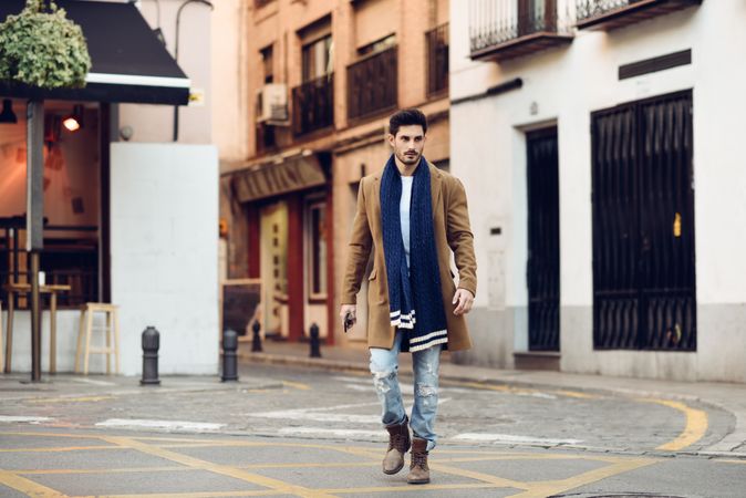 Man in scarf and coat walking through Spanish town