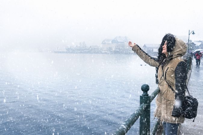 Woman reaching out to catch snowflakes outside near a lake