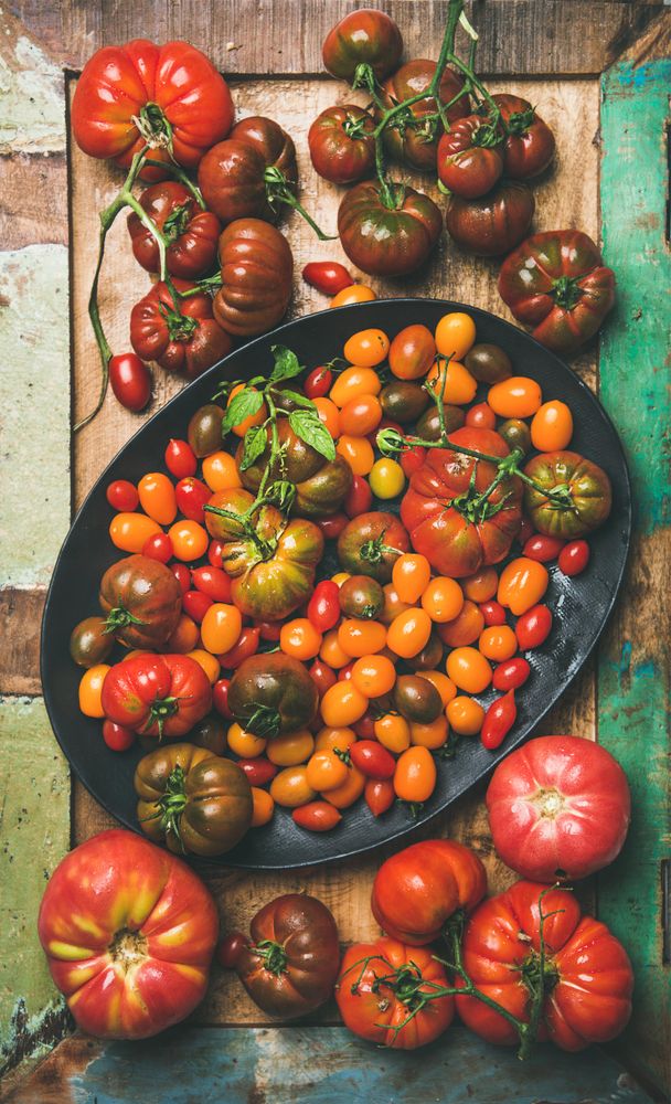 Assortment of different tomatoes in oval bowl, on wooden table, vertical composition