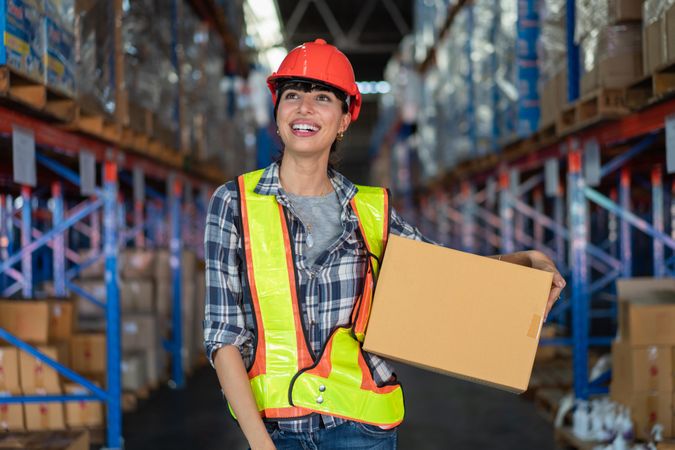 Woman in hard hat carrying in box in distribution center