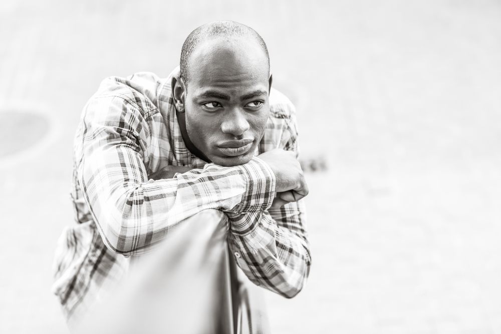 Monochrome picture of male in plaid shirt leaning on railing with listless expression