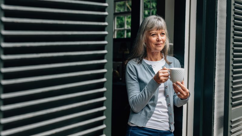 Smiling woman standing at the door with a coffee cup in hand