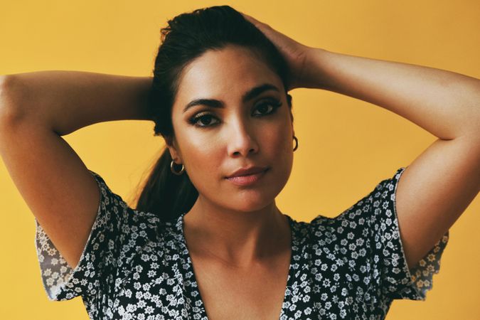 Headshot of Hispanic woman pulling her hair back into pony tail in yellow room