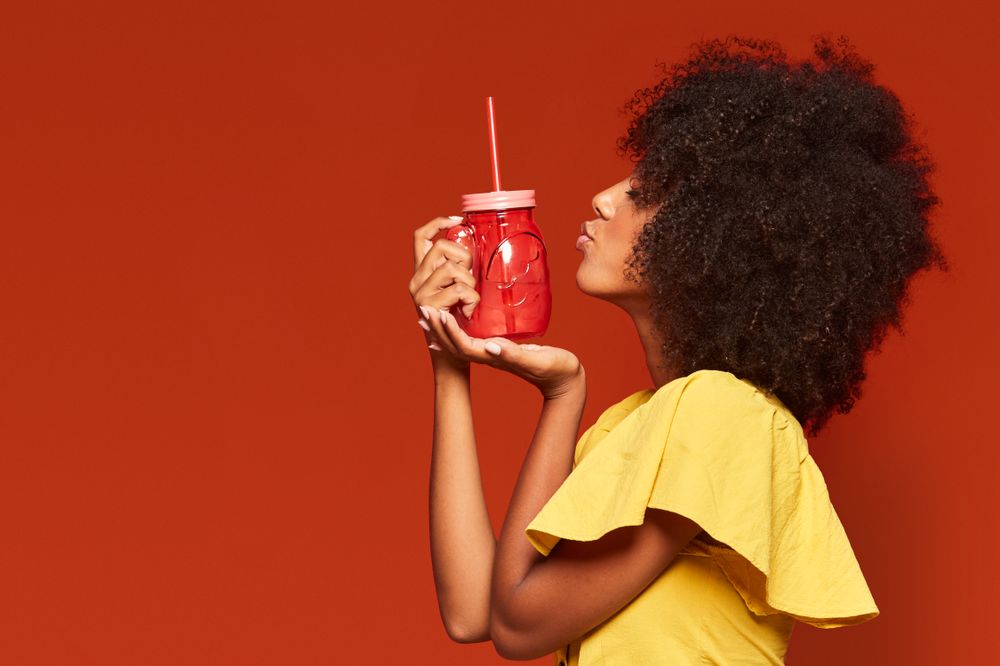 Charming bright Black woman drinking beverage