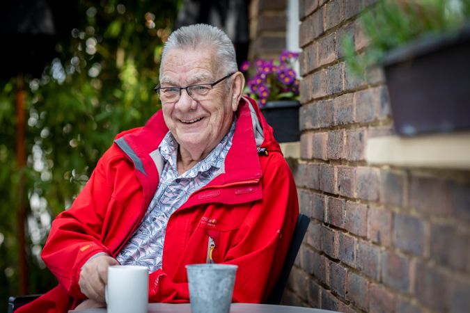 Calm and smiling older man sitting at outside cafe with coffee mug