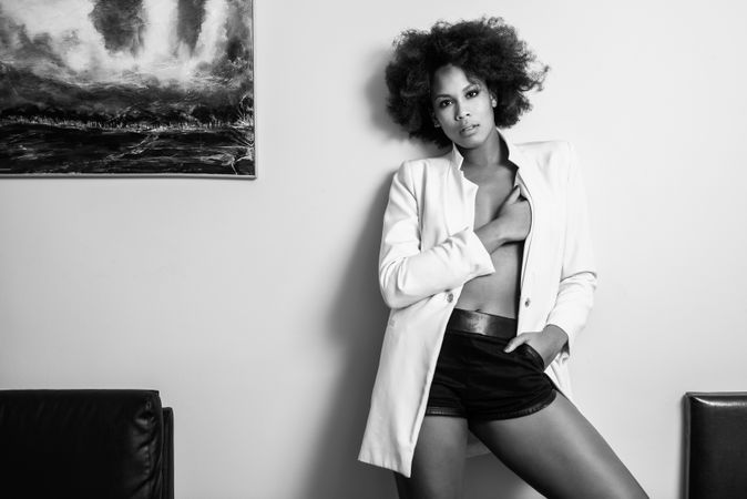 Monochrome shot of female with curly hair in pajamas standing against wall in home