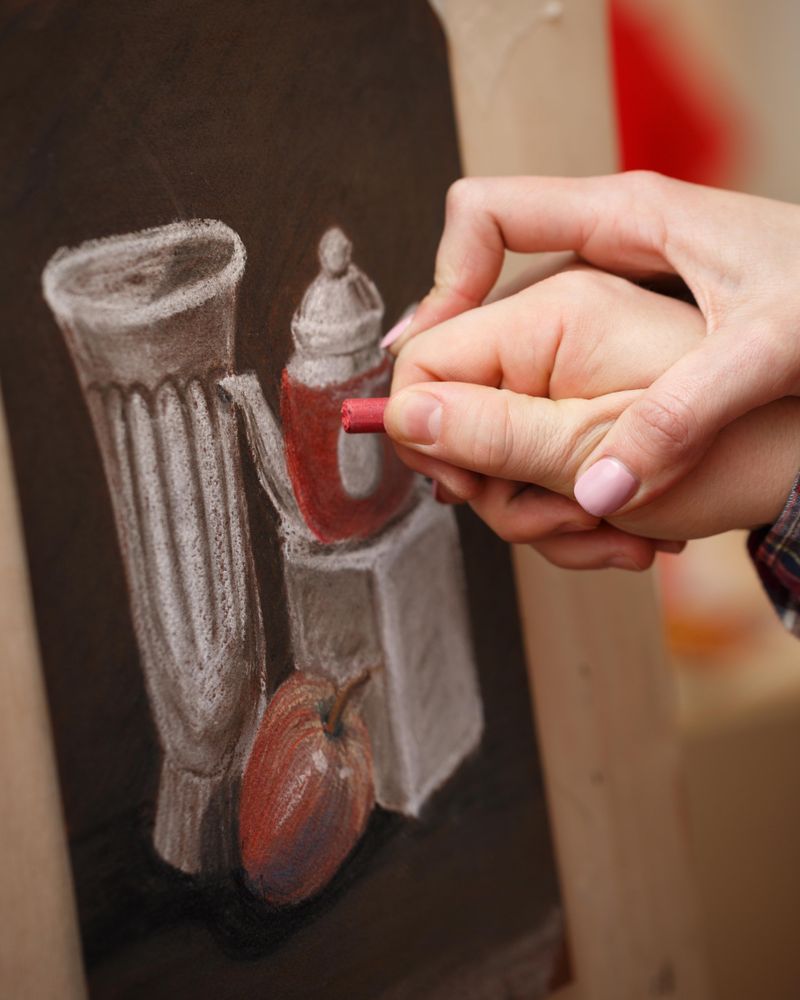 Hand of teacher showing technique student as he draws a still life of tea pot and apple