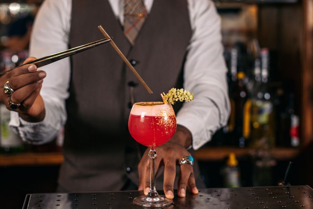 Close-up of an unrecognizable Black bartender pouring a cocktail and decorating it with garnish