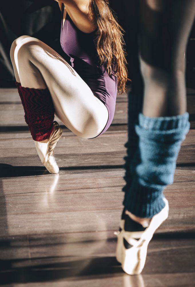 Crop shot of women training ballet in pointe shoes standing on tiptoes.