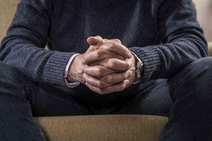 Close-up of a mature man's clasped hands on his lap.