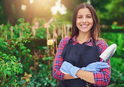 Confident woman pictured in a greenhouse with her arms crossed holding a a trowel
