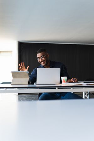 Black man video chatting on tablet near laptop in workplace