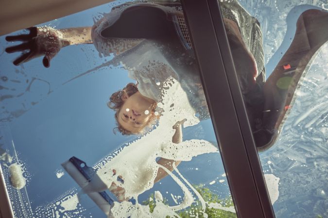Cheerful boy washing window of car