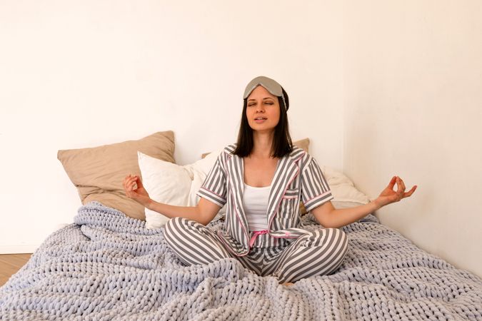 Woman meditating in bed in pajamas, peaceful expression.
