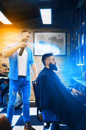 Barber spraying hair product on man’s hair, vertical