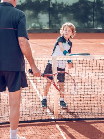 Active little boy practicing tennis with crop male instructor