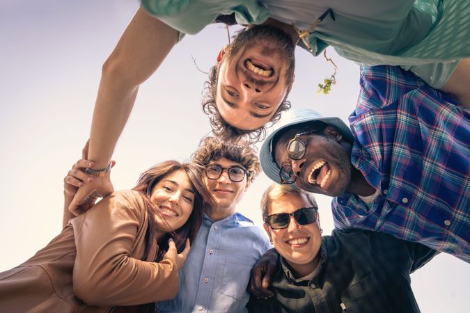 Low angle point of view shot of happy diverse friends in a huddle outdoors.