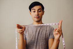 Hispanic male holding measuring tape between hands in beige studio shoot