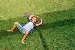 Boy screaming and lying on skateboard on grass