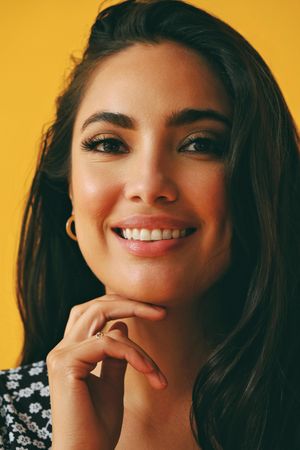 Happy Hispanic woman wearing dress standing in yellow room, vertical
