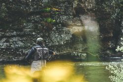 Confident man fishing with rod while standing in river stream