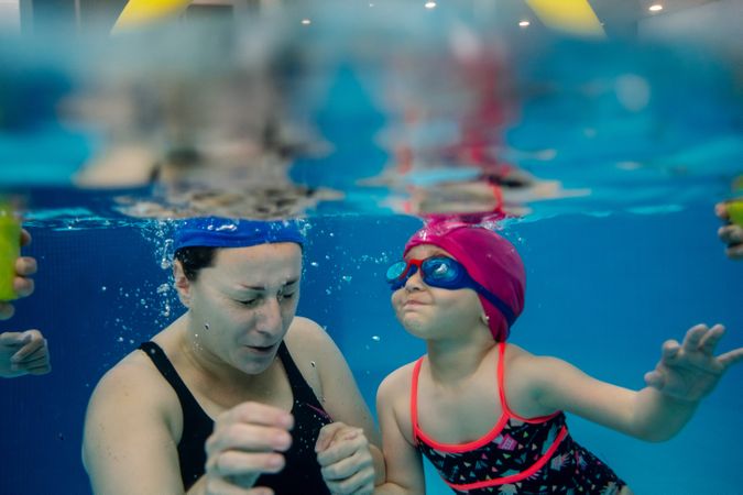 Cheerful girl underwater swimming in pool with mother
