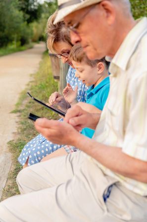 Grandchild and grandmother using a tablet outdoors on bench