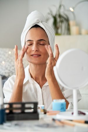 Delighted woman smearing anti aging cream under eyes