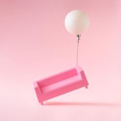 Pink sofa with Christmas bauble decoration on pink background with bauble floating side of sofa