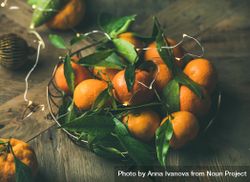 Freshly picked tangerines with leaves in wire bowl on wooden table 5zjMj5