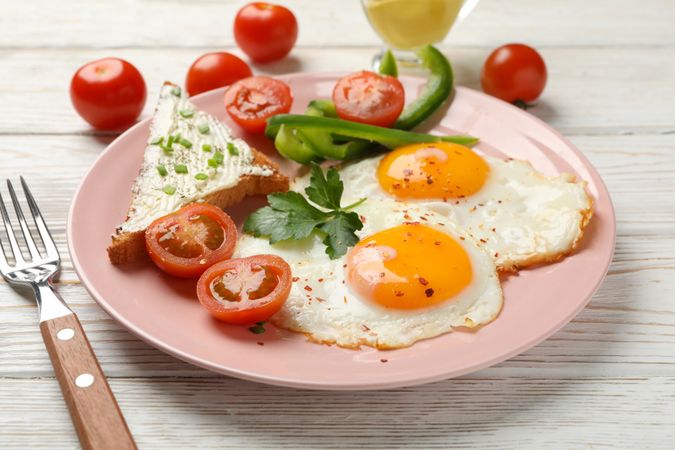 Two fried eggs with tomatoes and toast on pink plate