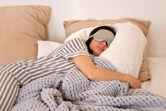 Woman sleeping deeply with eye mask in cozy bed.