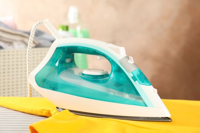 Iron and yellow t-shirt on ironing board, space for text