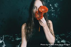 Studio portrait of woman with blue eyes holding gerbera flowers against floral background 0LW1Ab
