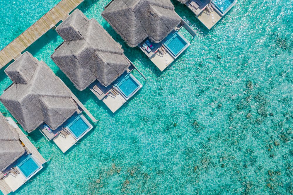 Aerial shot of patio pool of thatched beach villas in the sea